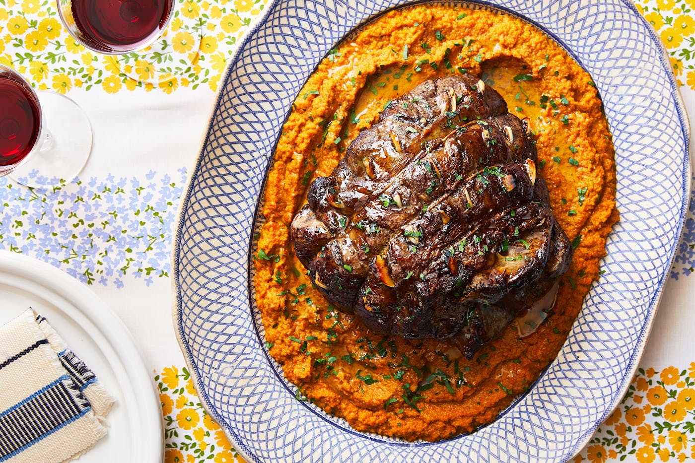 A roasted leg of lamb atop a vibrant orange vegetable spread, set on a platter. 