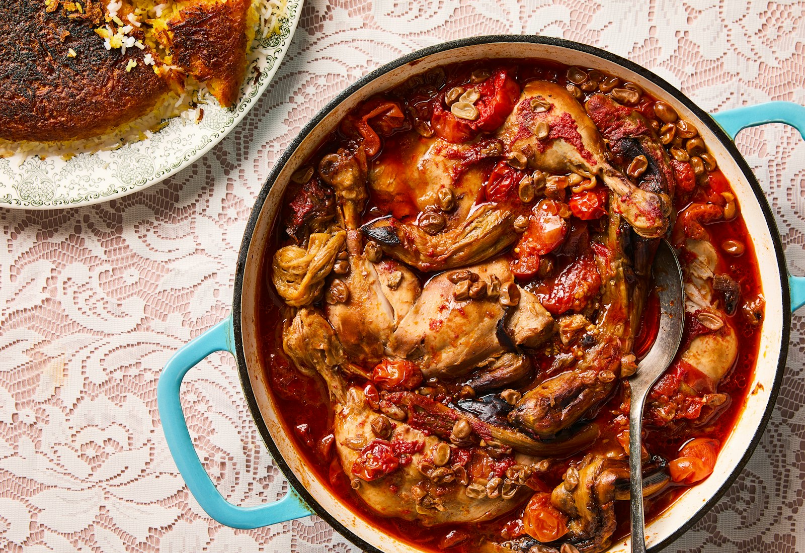 A blue-handled pan of braised chicken with tomatoes, eggplants and sour grapes.