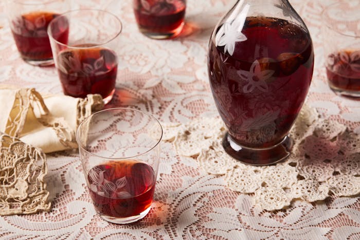 Shot glasses of bright red sour cherry infused vodka on a lacy, light pink tablecloth.