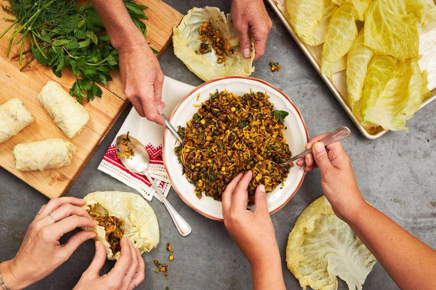 Festive dinner scene with three people stuffing cabbage leaves with rice mixture and herbs.