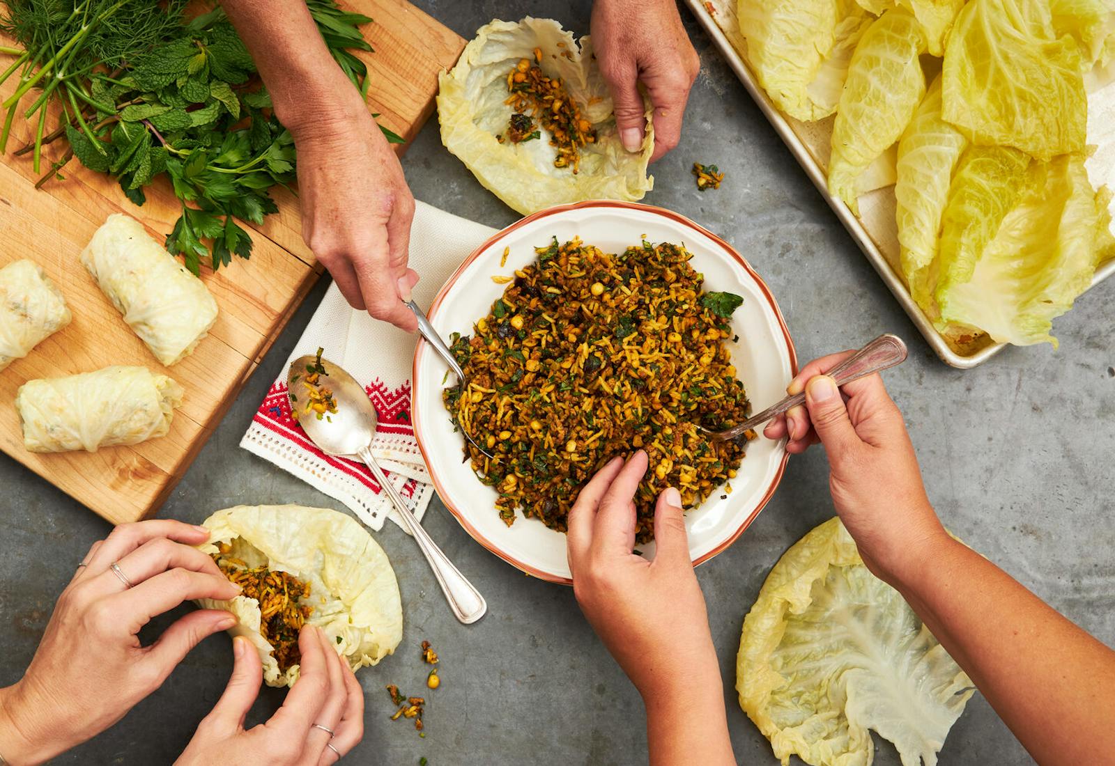 Festive dinner scene with three people stuffing cabbage leaves with rice mixture and herbs.