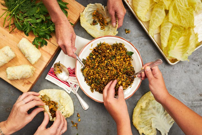Festive dinner scene with three people stuffing cabbage leaves with rice mixture and herbs.