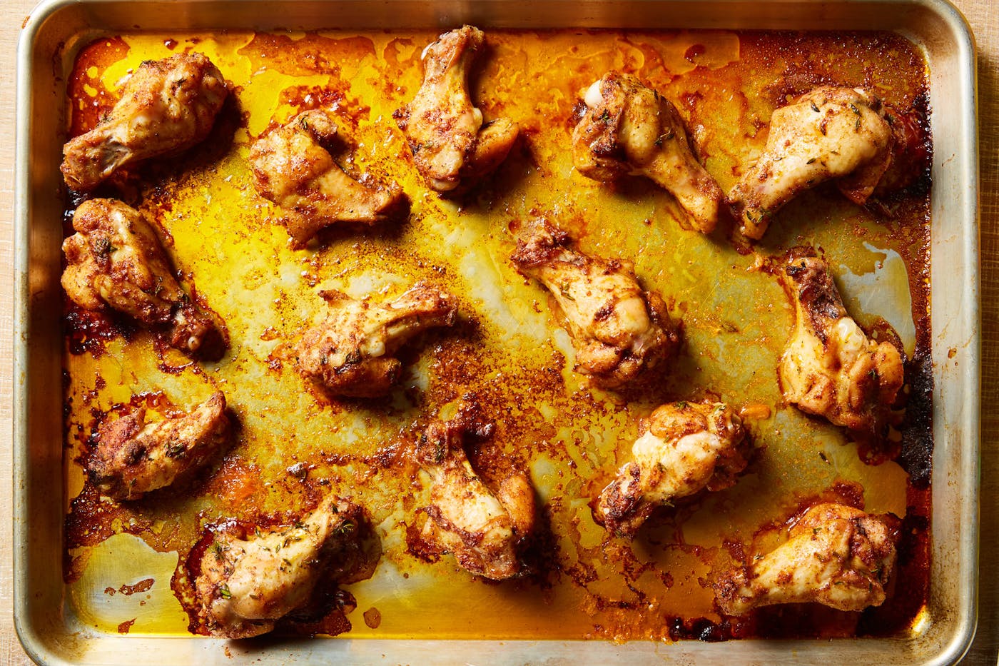 Chicken wings in their juices on baking sheet.