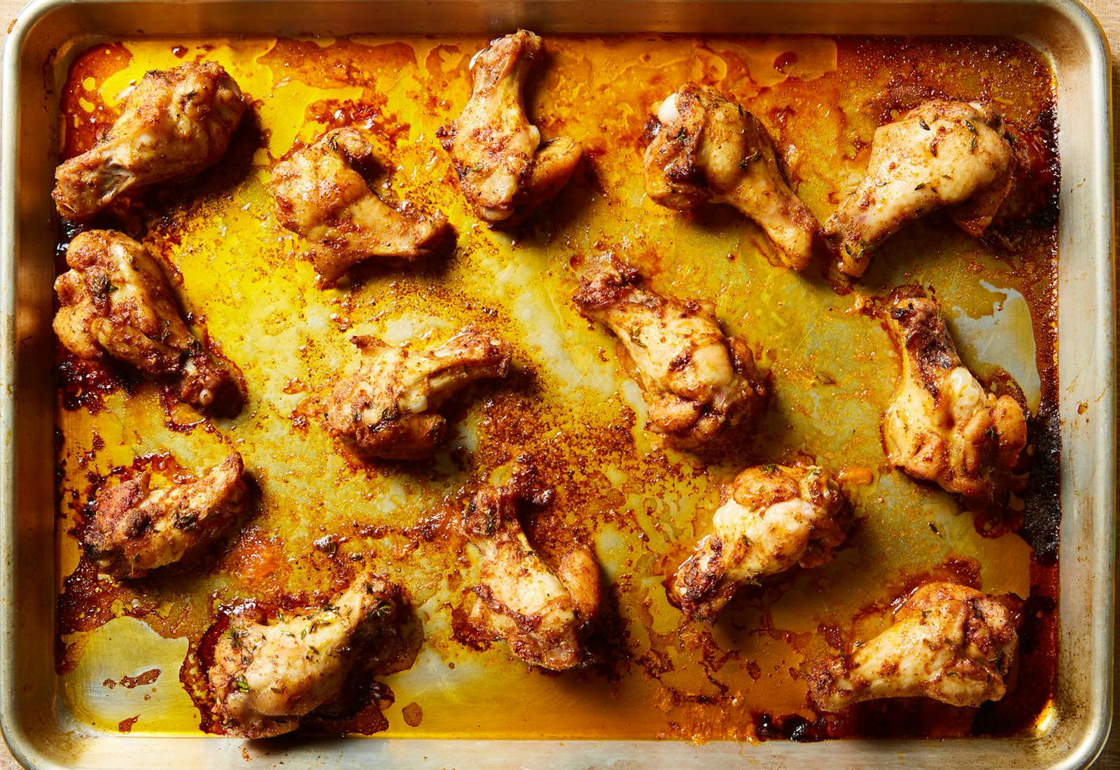 Chicken wings in their juices on baking sheet.