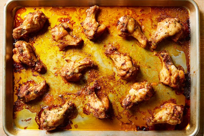 Chicken wings in their juices on baking sheet.
