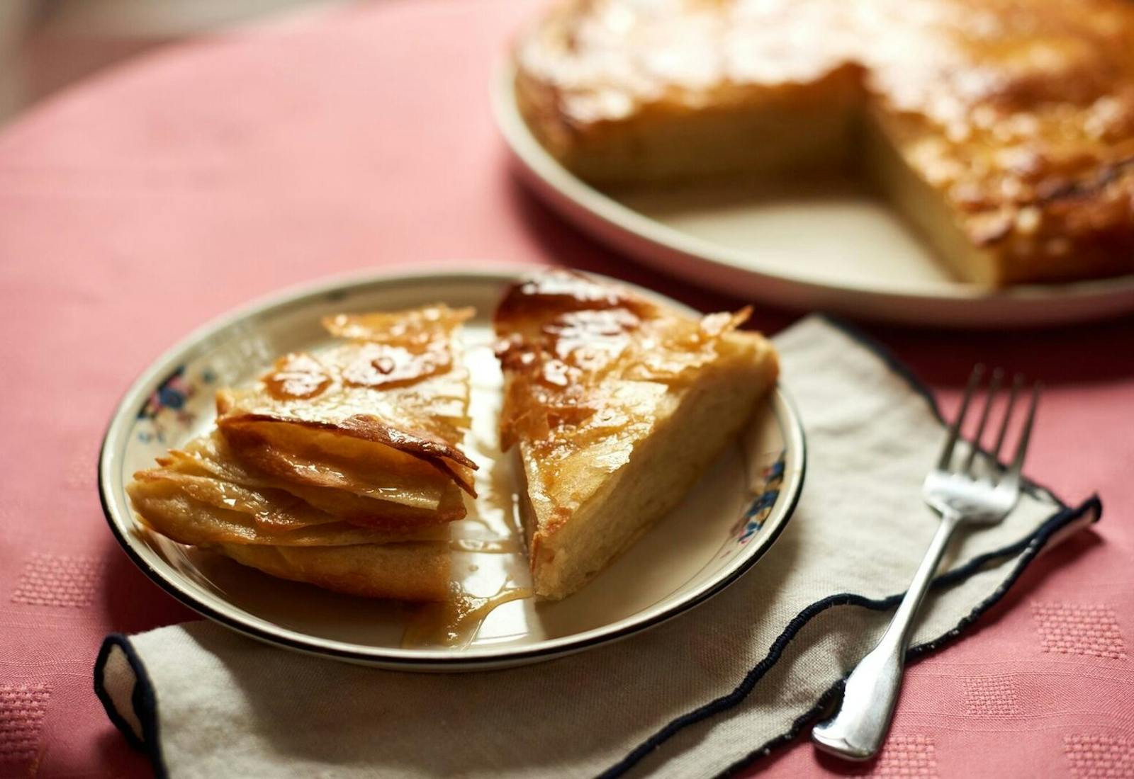 Slices of sabaya on small dish alongside whole cake on large white dish, atop pink tablecloth.