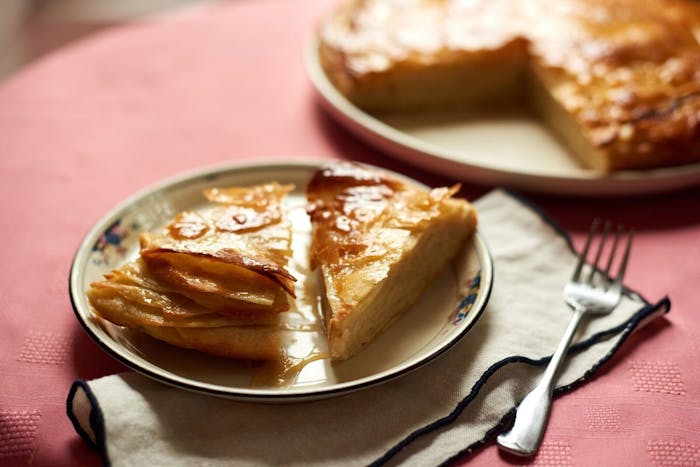 Slices of sabaya on small dish alongside whole cake on large white dish, atop pink tablecloth.
