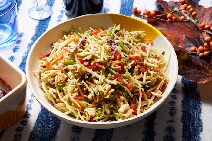 Broccoli slaw salad in white bowl, bottle of red wine with wine glass, atop blue and white tablecloth.