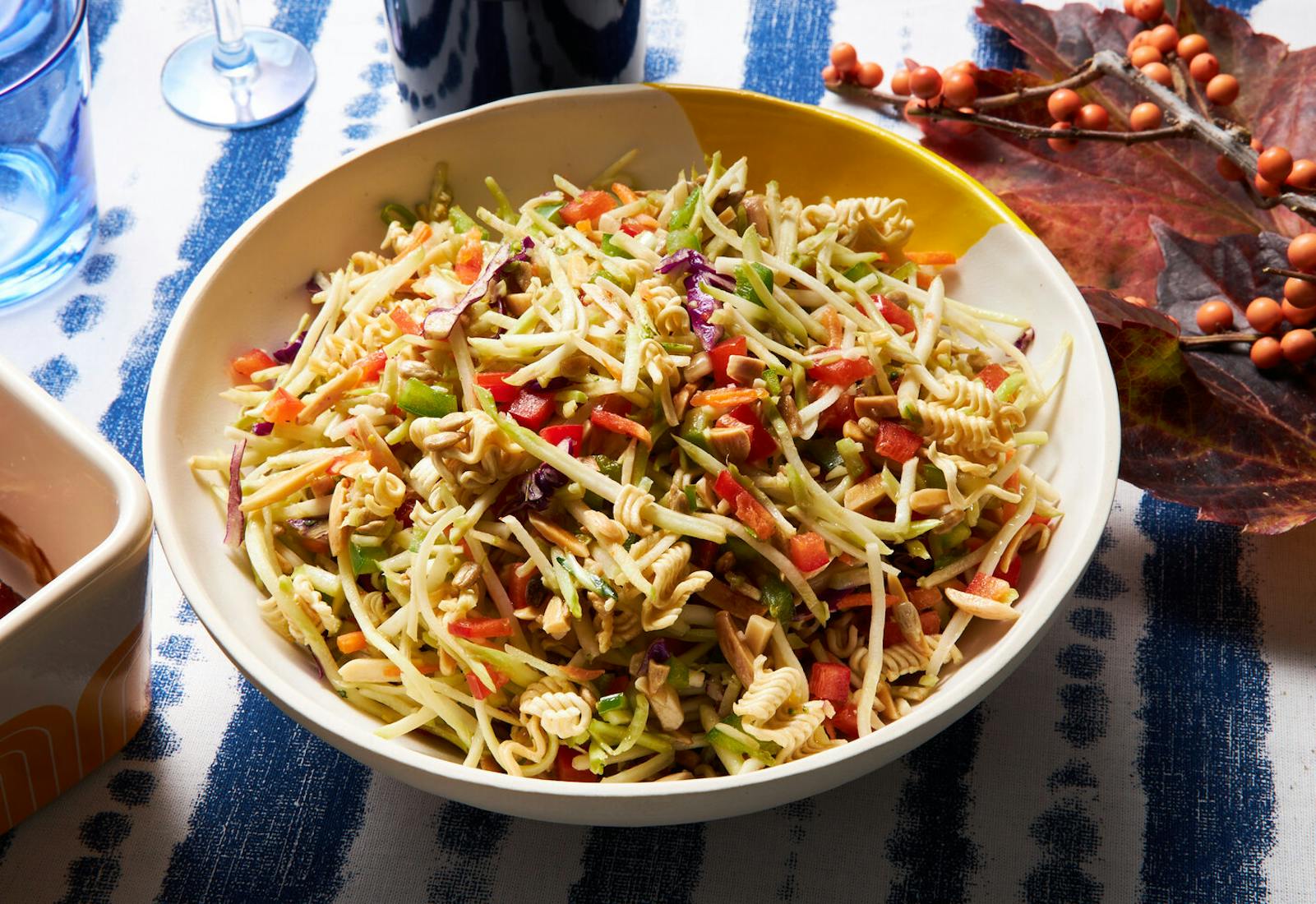 Broccoli slaw salad in white bowl, bottle of red wine with wine glass, atop blue and white tablecloth.