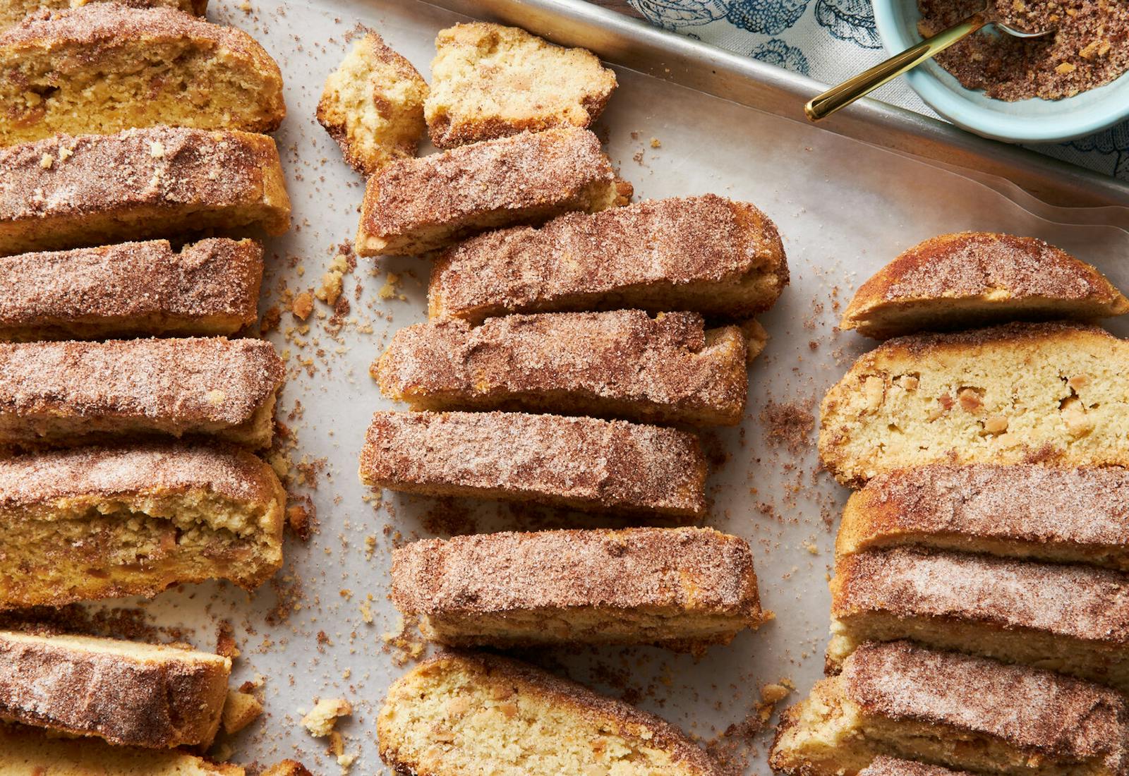 Pieces of mondel bread on baking sheet, bowl with cinnamon sugar.