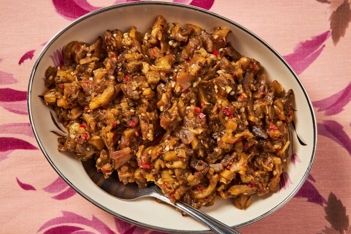 Roasted eggplant salad in large bowl atop pink floral tablecloth.