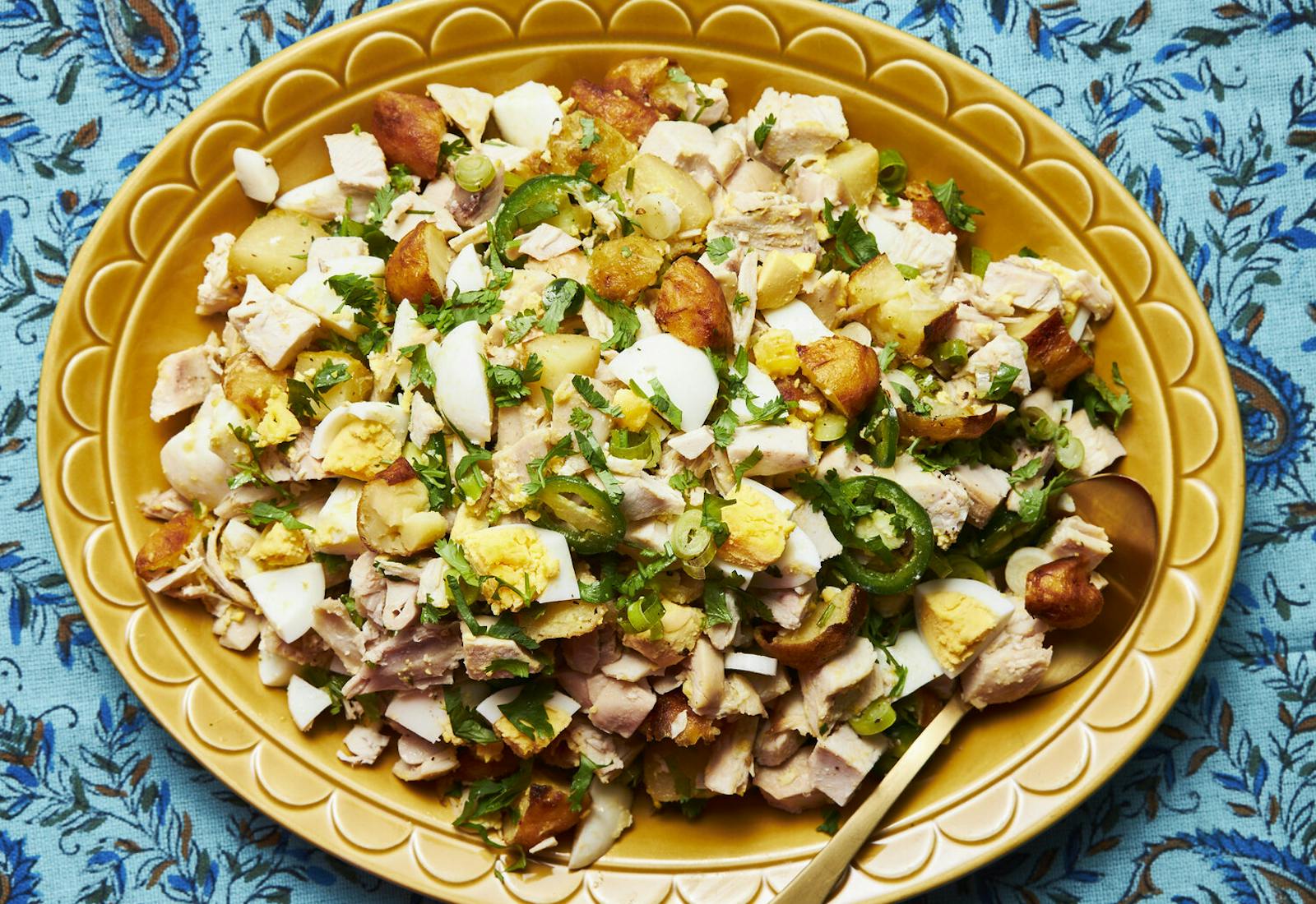 Shabbat salad garnished with chopped parsley on yellow serving dish atop blue feather-printed tablecloth.