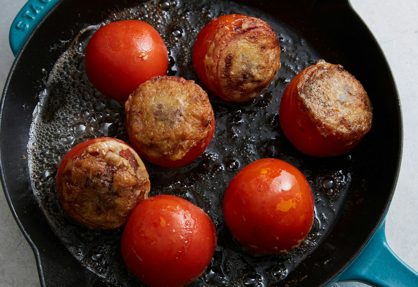 Tomatoes reinvades cooking on blue enameled cast iron skillet.