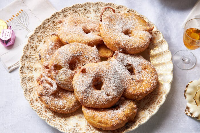 Fritters dusted with powdered sugar, gelt and dreidel atop menorah-print napkin.