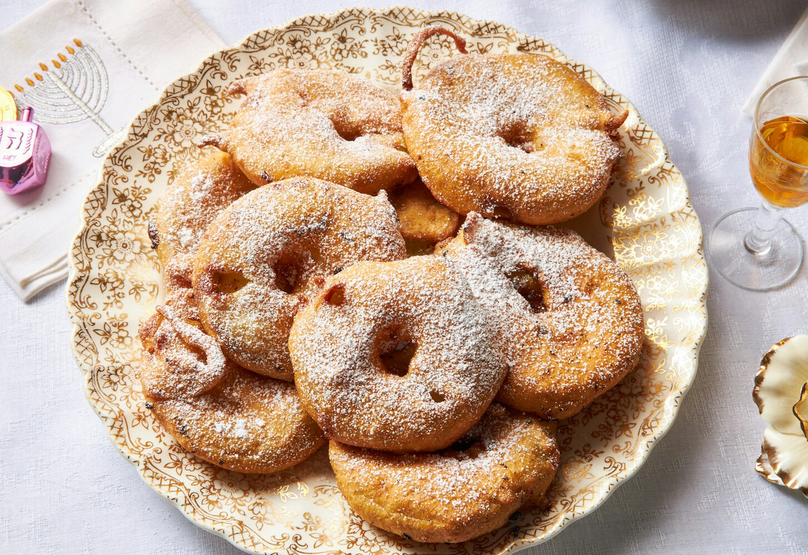 Fritters dusted with powdered sugar, gelt and dreidel atop menorah-print napkin.