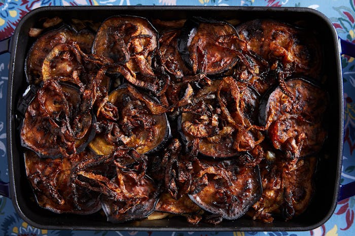 Almoronia with sautéed onions in dark blue casserole dish atop blue tablecloth.
