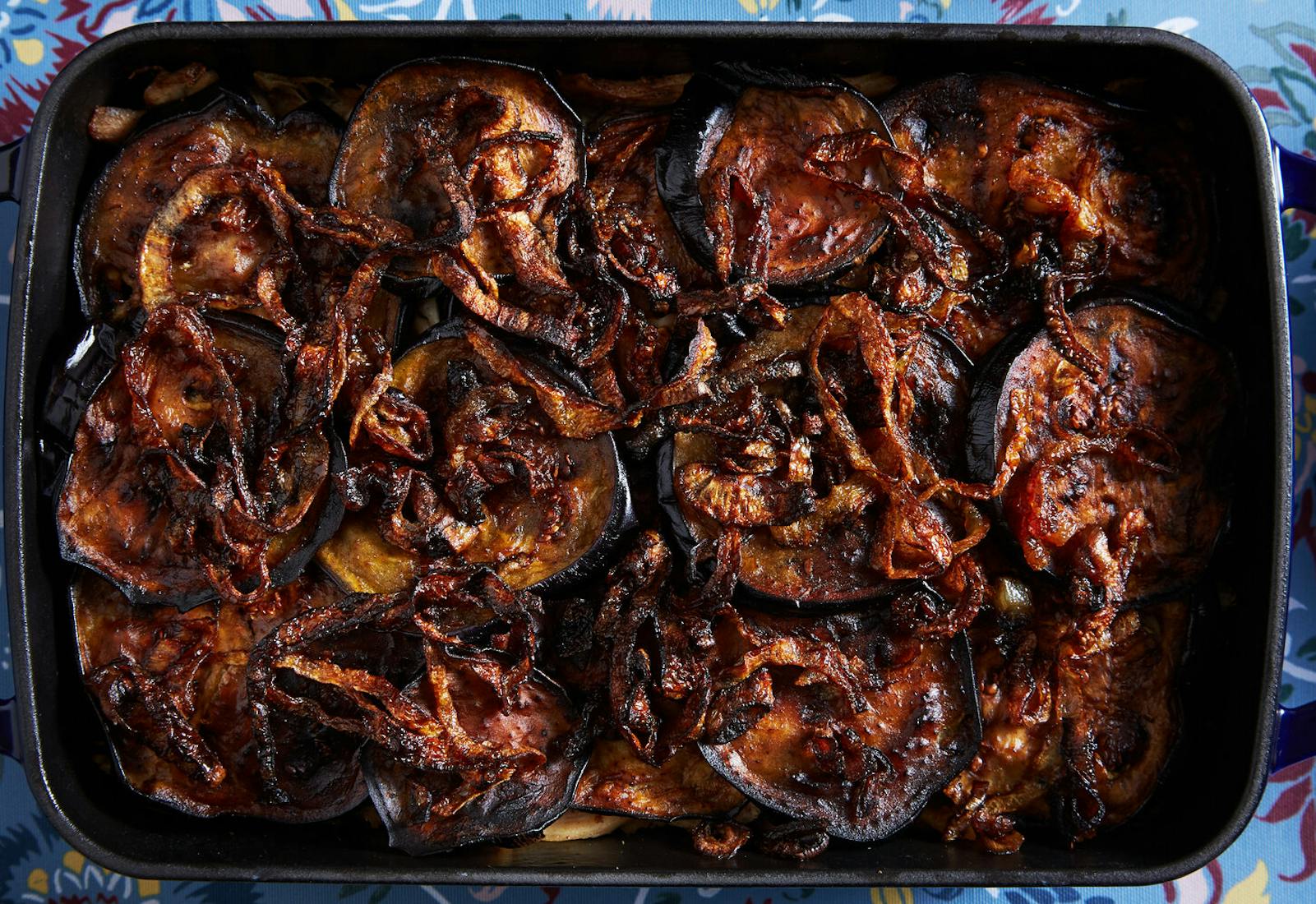 Almoronia with sautéed onions in dark blue casserole dish atop blue tablecloth.