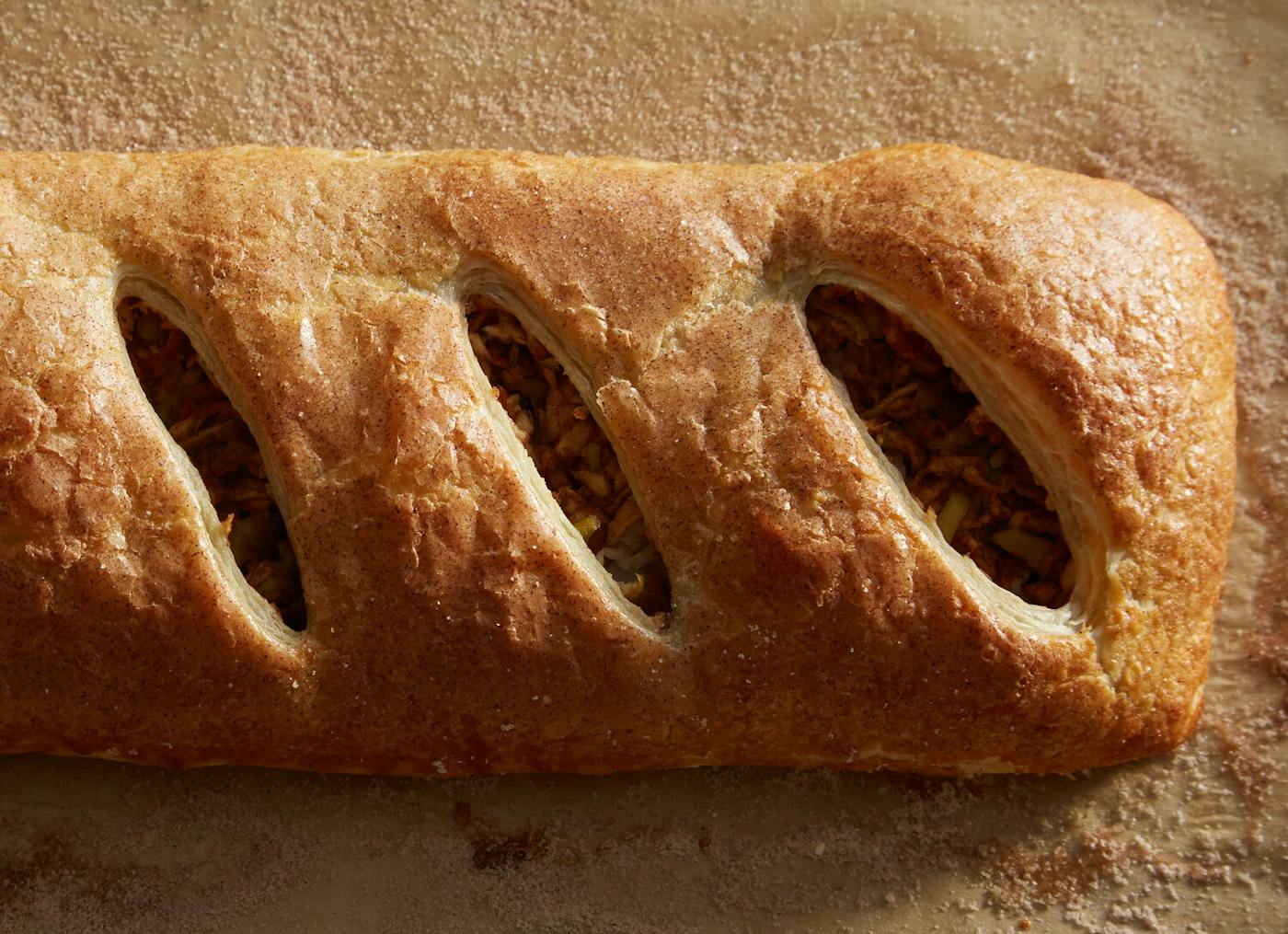 Golden apple strudel atop cinnamon-sugar covered parchment paper.