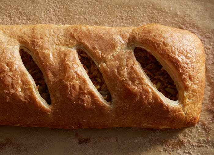 Golden apple strudel atop cinnamon-sugar covered parchment paper.