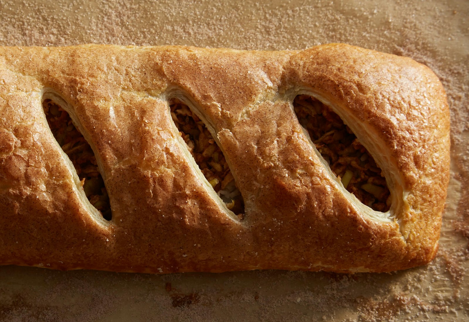 Golden apple strudel atop cinnamon-sugar covered parchment paper.