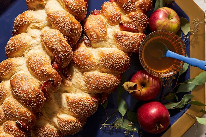 Sweet challah with bowl of honey and apples with leaves atop blue and gold platter.