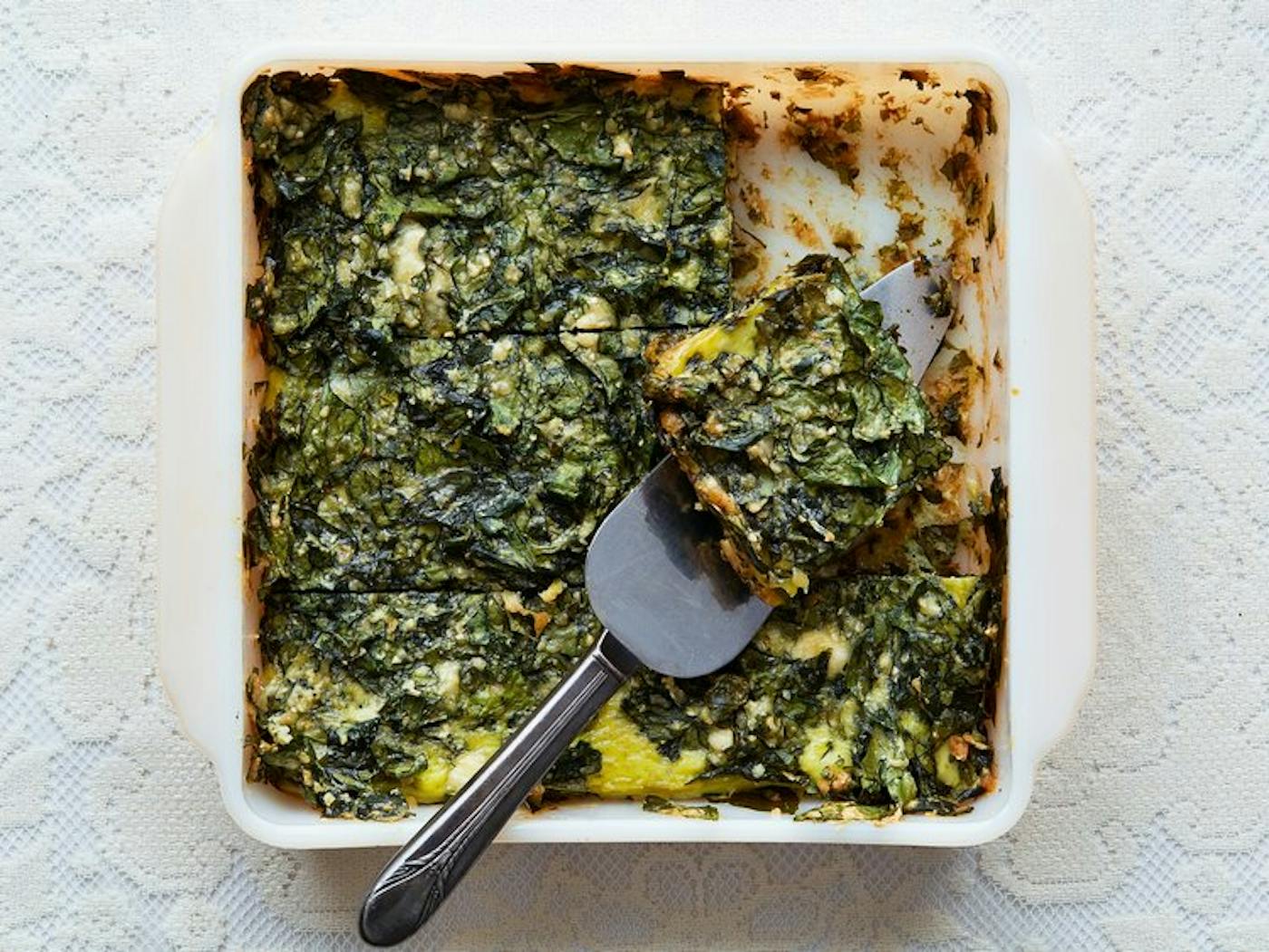 Spinach fritada in white casserole dish with pie server.