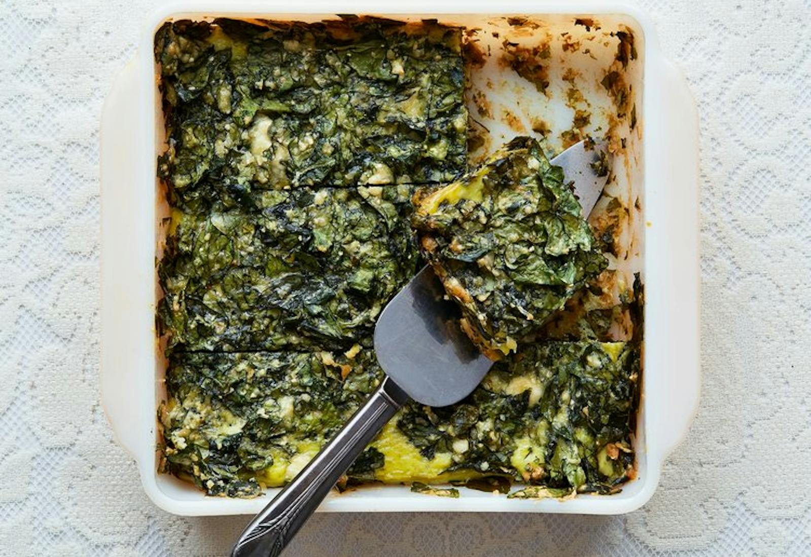 Spinach fritada in white casserole dish with pie server.