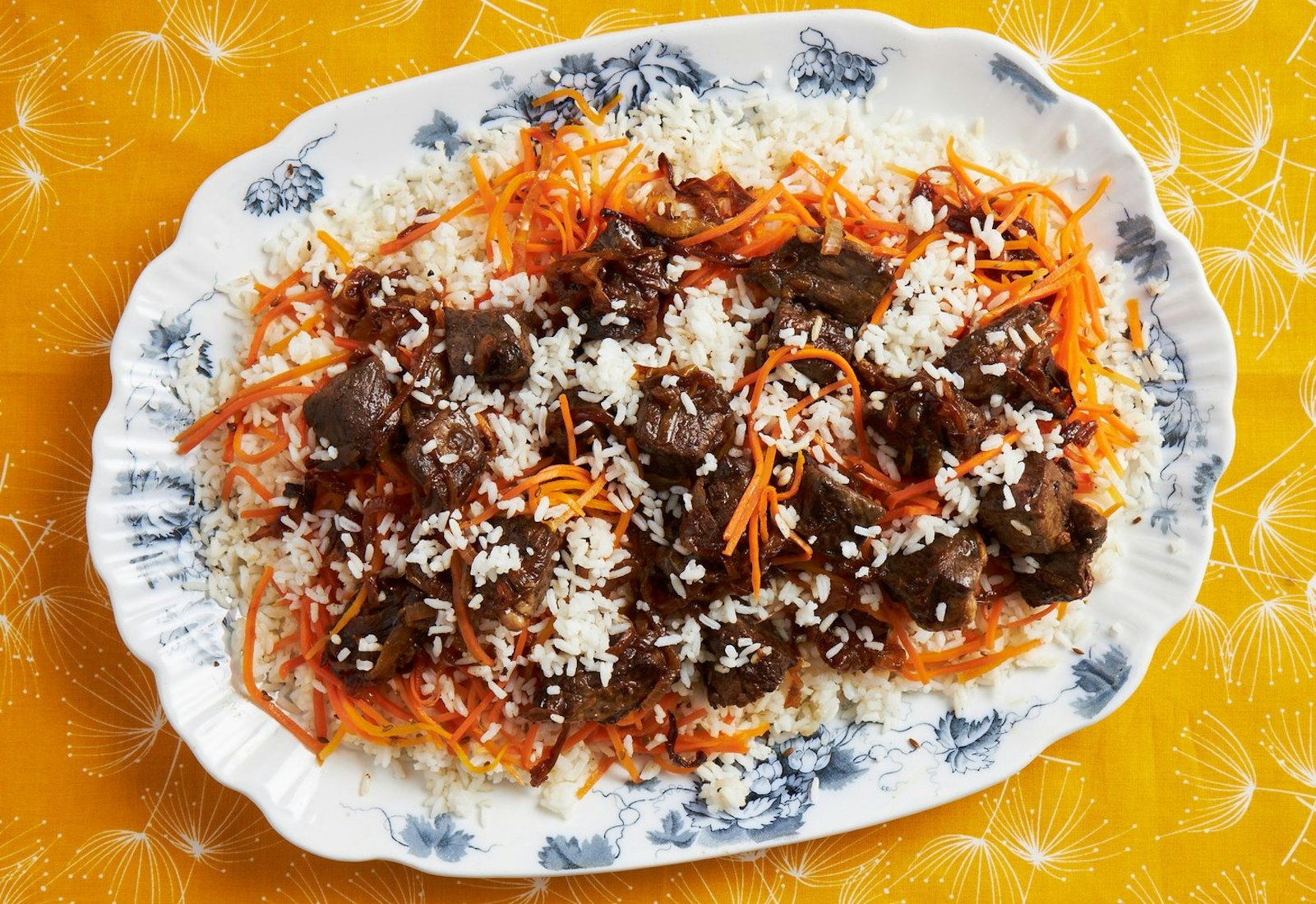Plov on floral dish atop bright orange tablecloth.