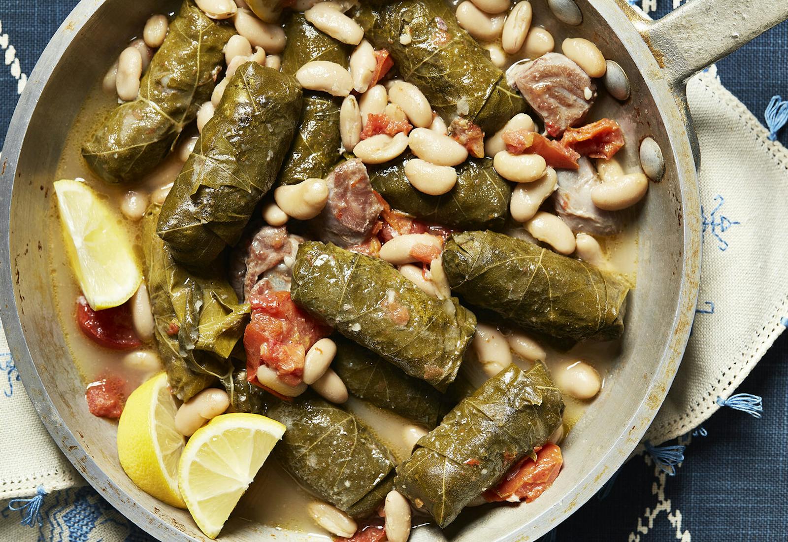 Yaprakes de oja with lemon wedges in a saute pan atop blue tablecloth.