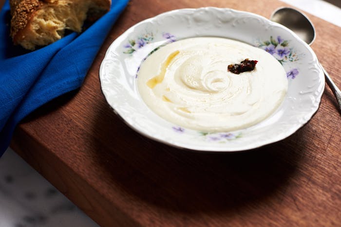 Mom with drizzle of lemon juice in floral bowl alongside challah in blue cloth napkin atop wooden board.