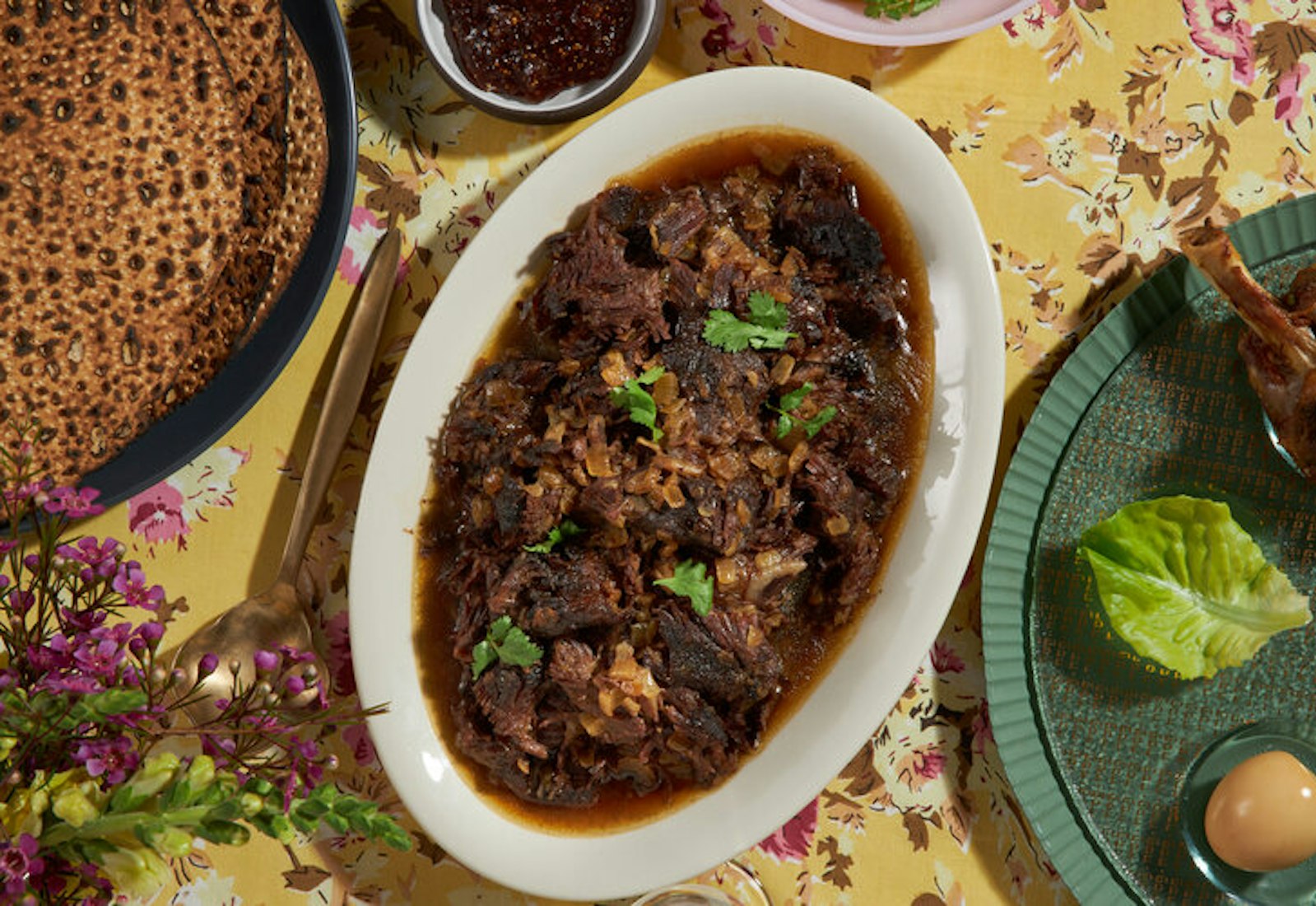 Braised beef cheeks with cilantro, round challah, fresh flowers and passover plate.