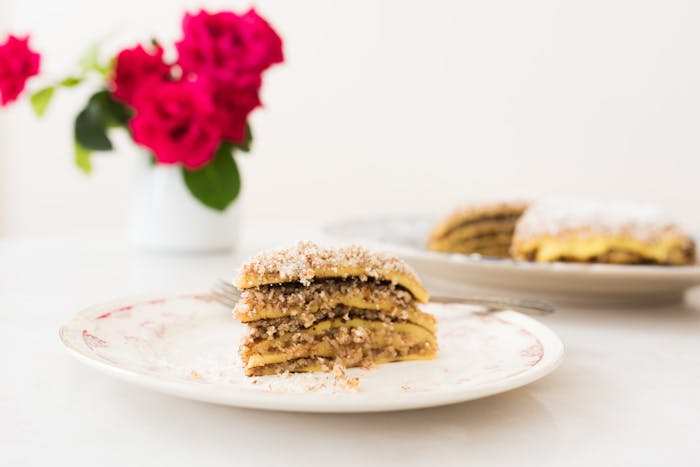 Slice of csusztatott palacsinta with whole cake in background along with pink roses.