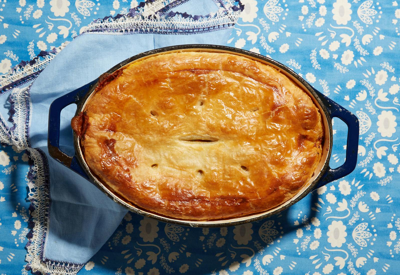 Cholent pot pie in cast iron casserole dish atop blue floral tablecloth with blue napkin.