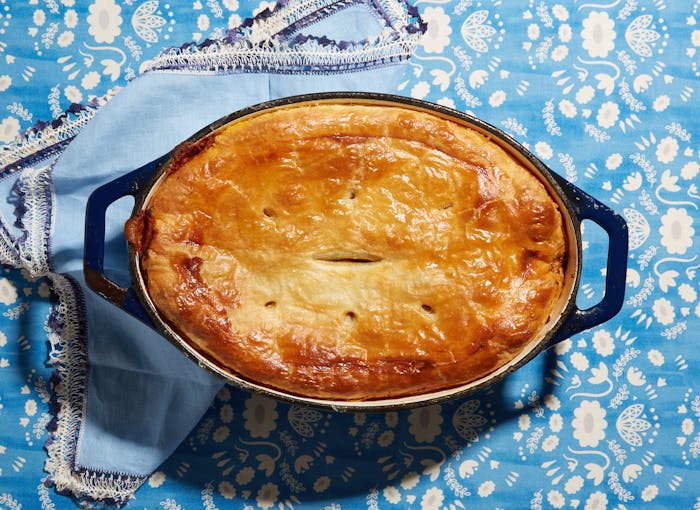 Cholent pot pie in cast iron casserole dish atop blue floral tablecloth with blue napkin.