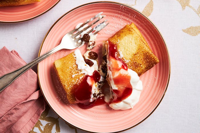 Nalesniki with jam and sour cream on salmon plate atop white and gold tablecloth.