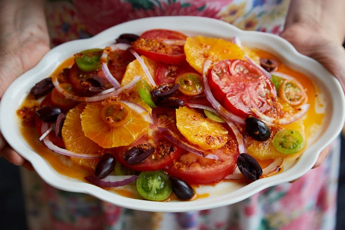 Chef holding tomato and citrus salad on white plate.