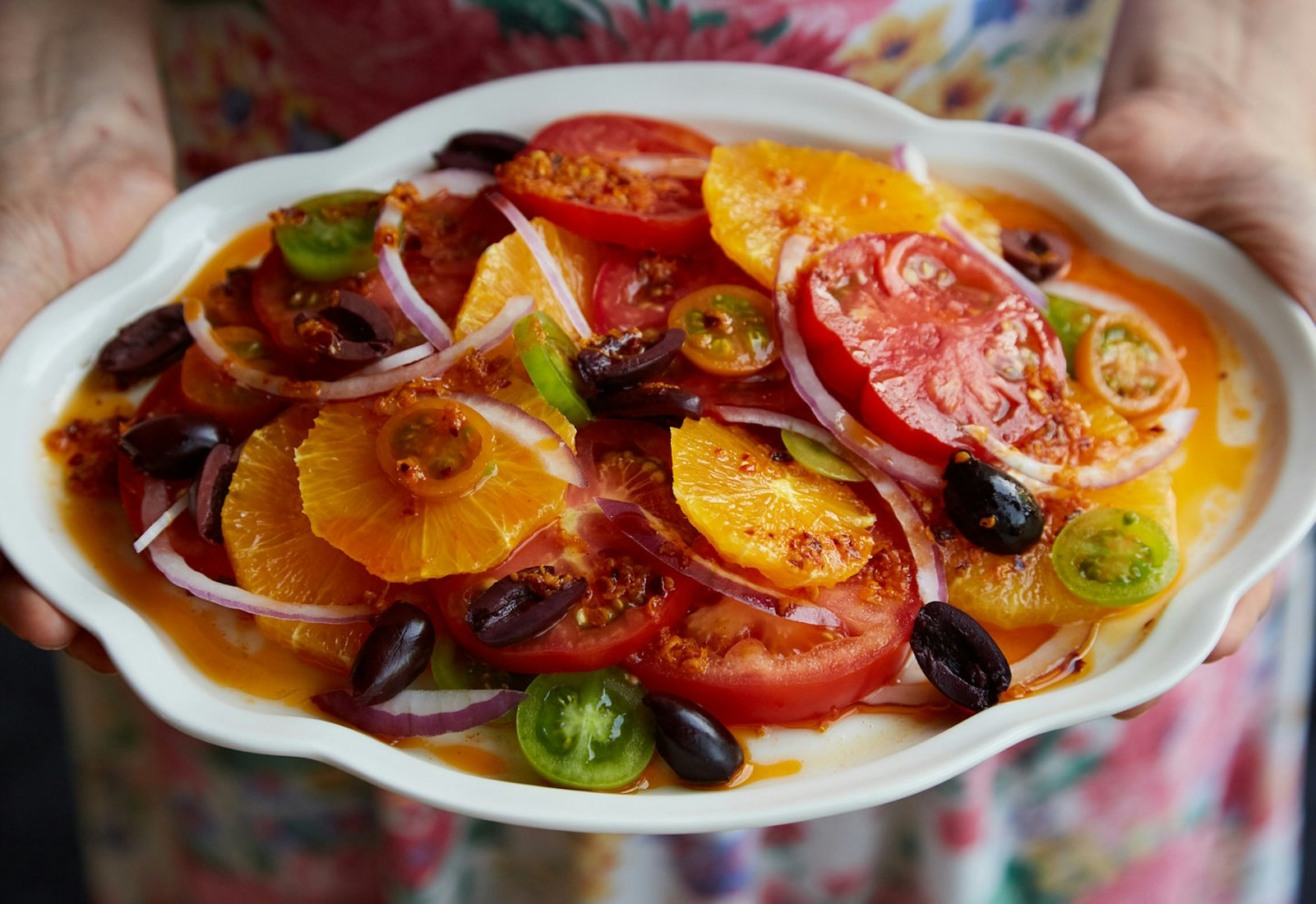 Chef holding tomato and citrus salad on white plate.