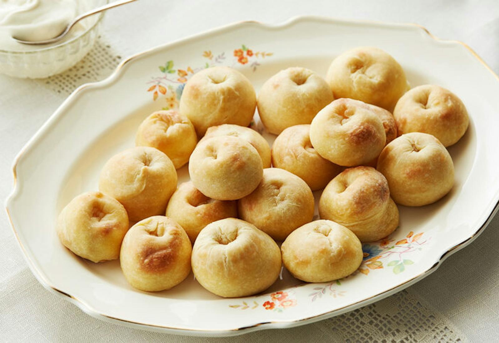 Knishes piled onto a floral serving dish, side of sour cream.