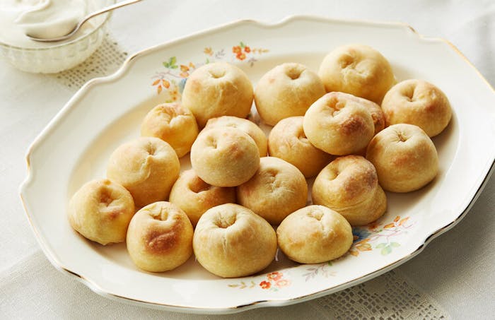 Knishes piled onto a floral serving dish, side of sour cream.
