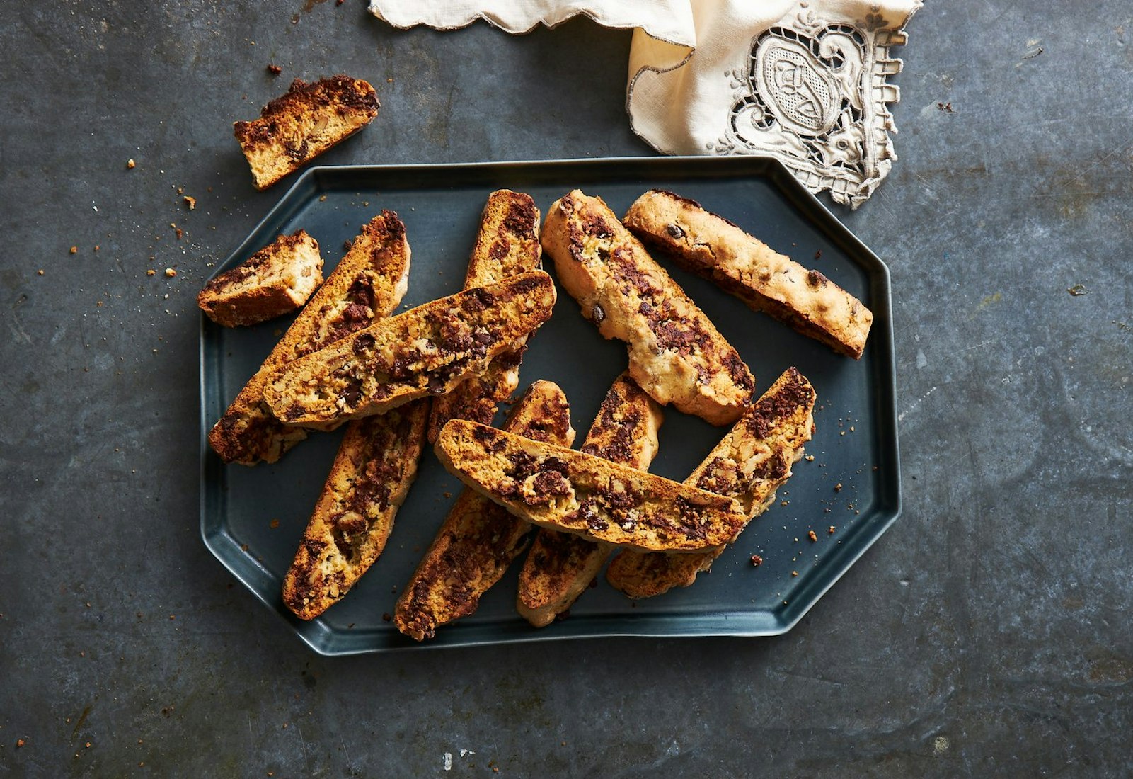 Mandel bread cookies with chocolate chips on black plate atop gray background.
