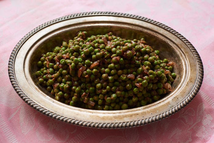 Peas with allspice in bronze serving bowl atop pink tablecloth.