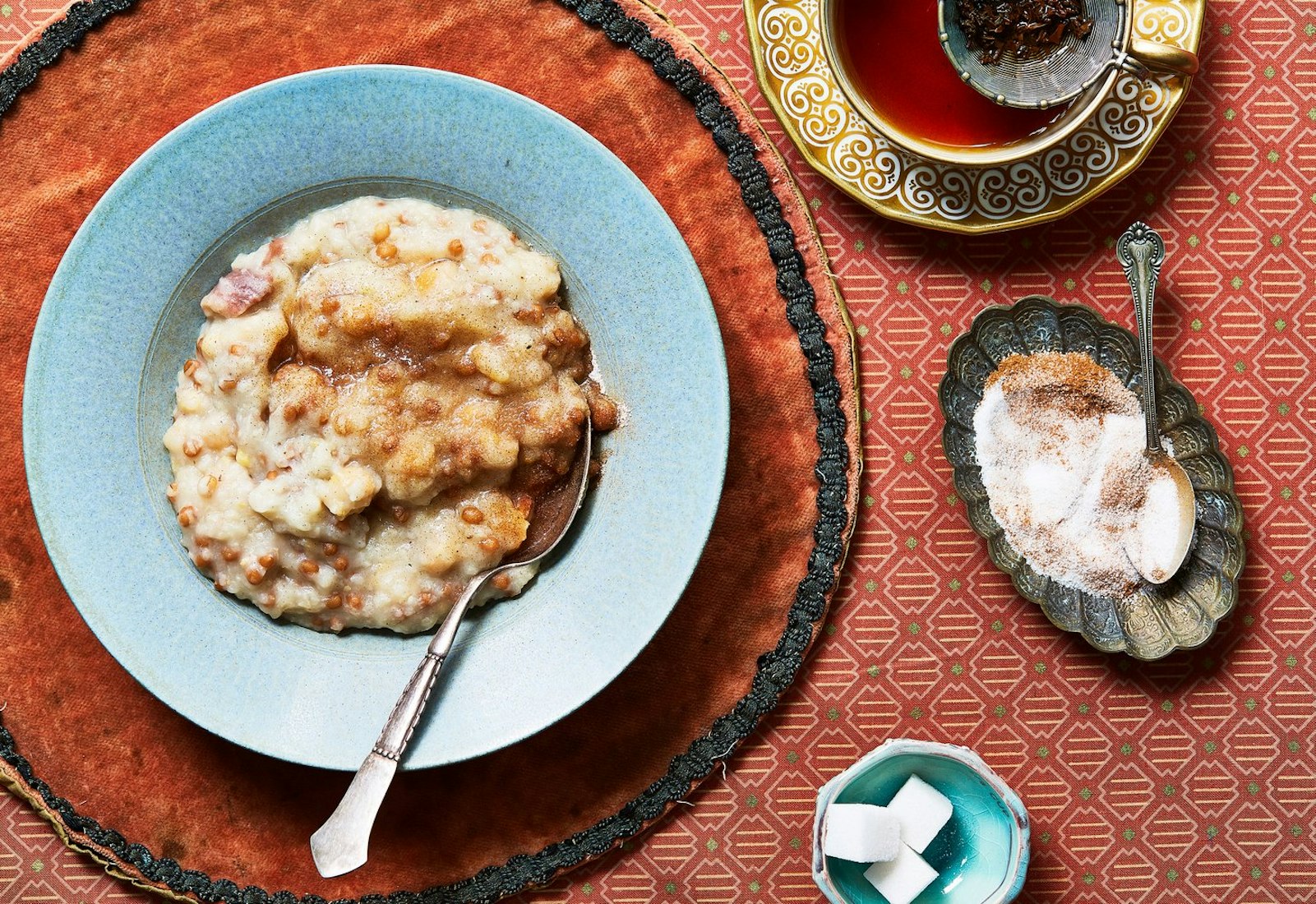 Halim sprinkled with sugar and cinnamon and hot tea, atop red patterned cloths.