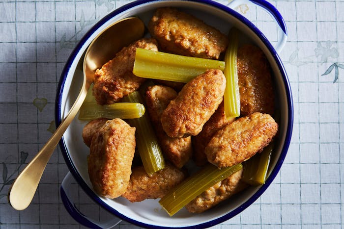 Chicken meatballs with celery in blue and white casserole dish atop grid-patterned tablecloth.
