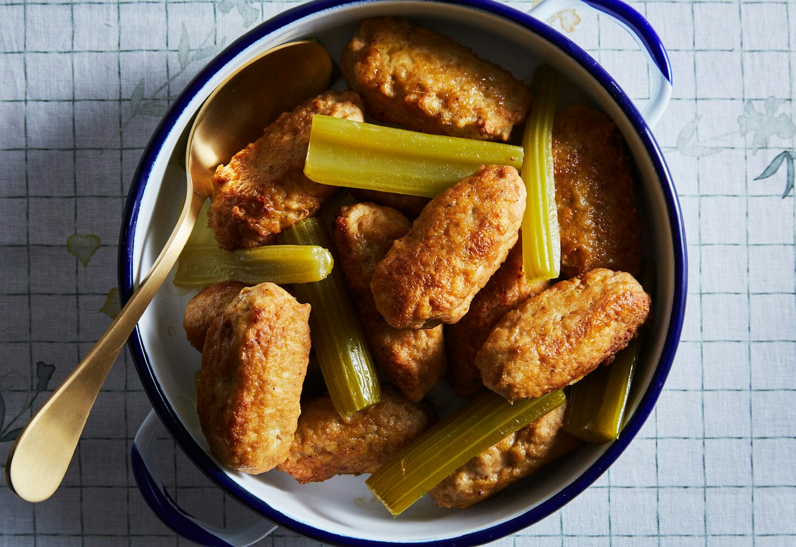 Chicken meatballs with celery in blue and white casserole dish atop grid-patterned tablecloth.