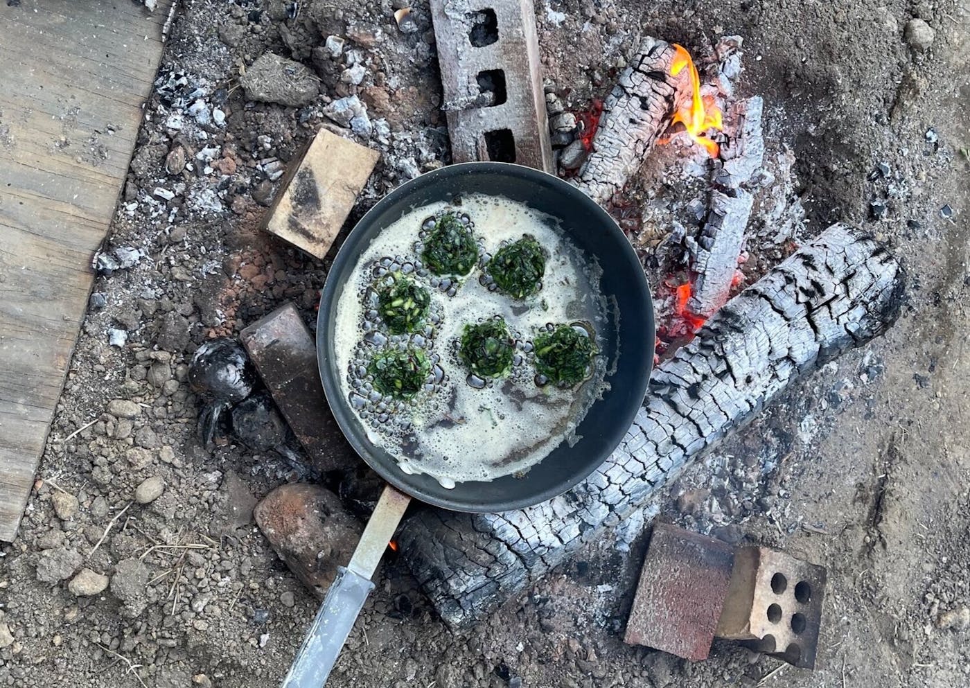Outdoor campfire scene with pan of fritters frying in oil. 