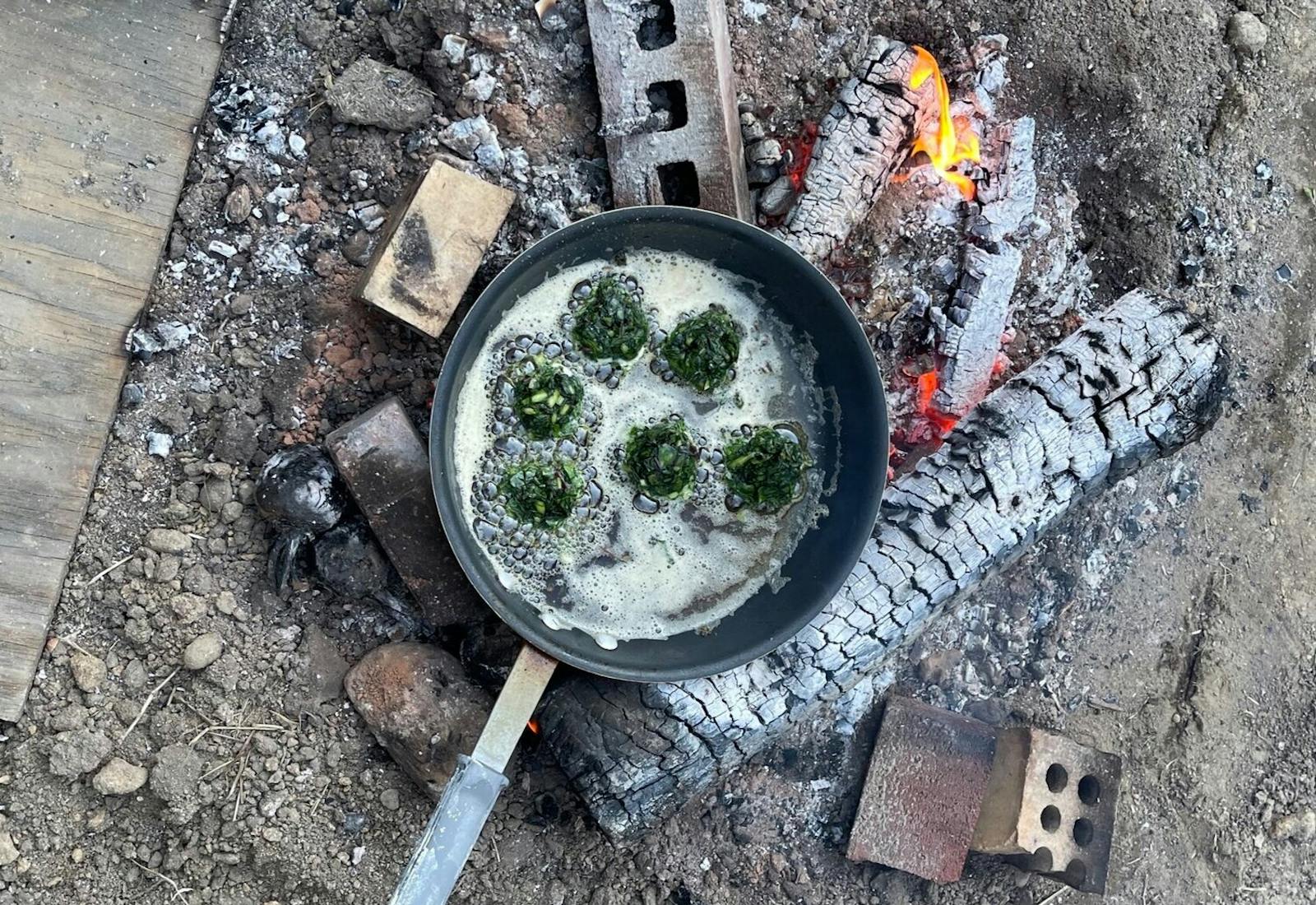 Outdoor campfire scene with pan of fritters frying in oil. 