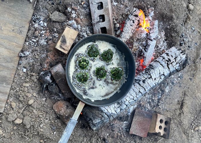 Outdoor campfire scene with pan of fritters frying in oil.