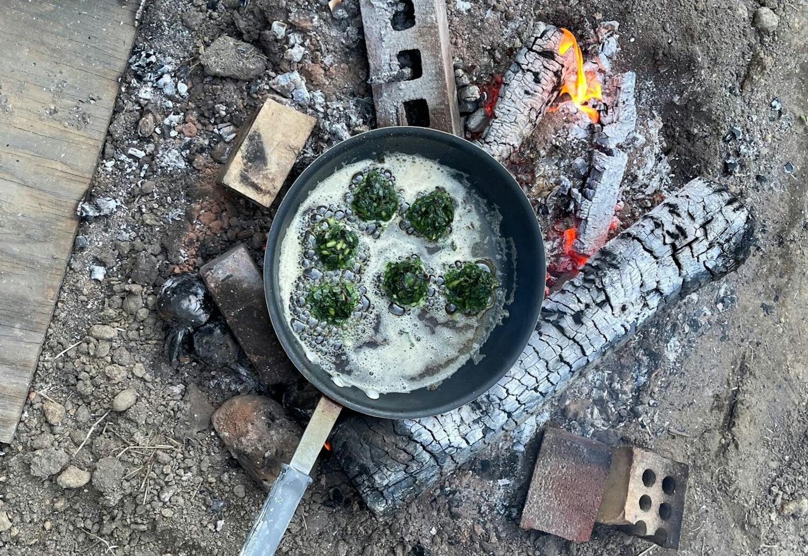 Outdoor campfire scene with pan of fritters frying in oil.
