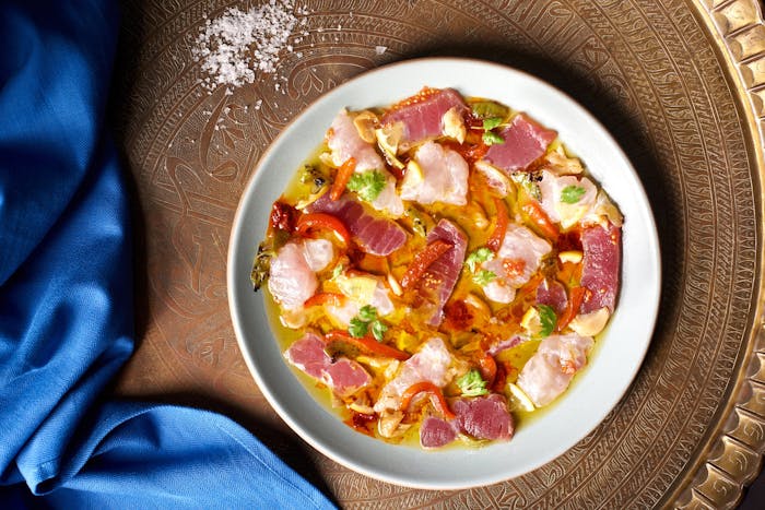 Spicy Moroccan fish crudo atop metal platter with sprinkle of coarse salt.
