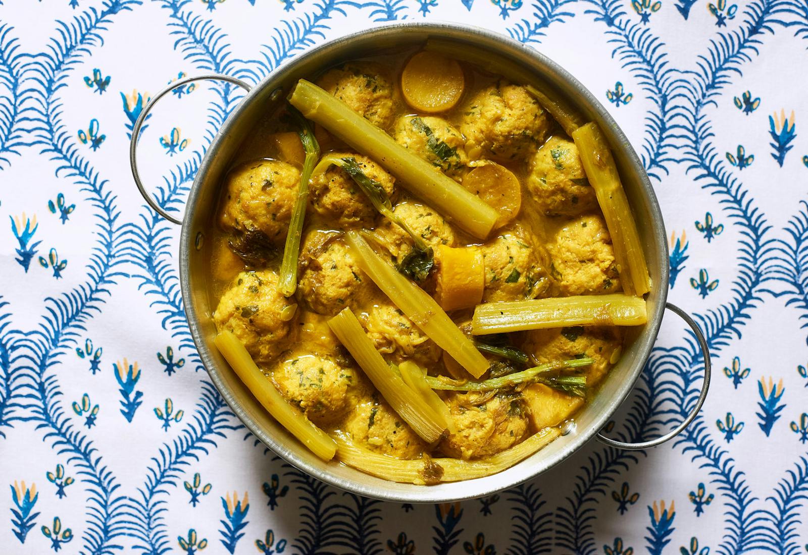 Moroccan turmeric chicken in metal pot atop blue and white tablecloth.
